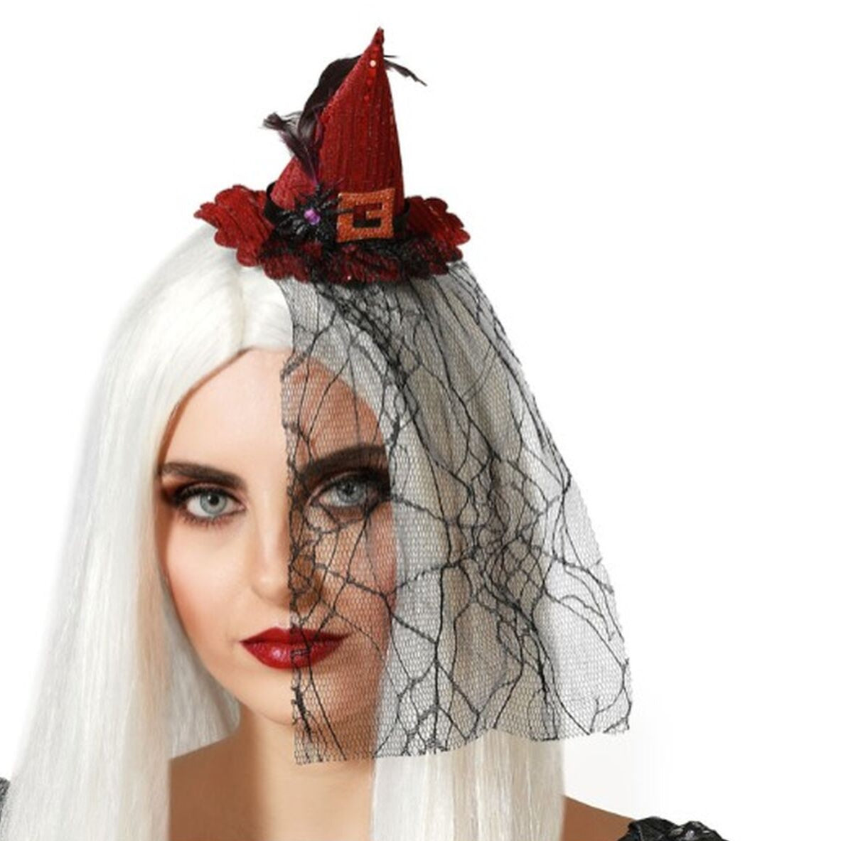 En kvinna med vitt hår och intensiv makeup bär ett rött, glittrigt häxdiadem med ett svart, spindelnätsmönstrat tyg som fungerar som en slöja över ena halvan av ansiktet.