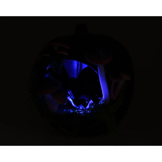 Den mörklila halloweenpumpan fotograferad i mörker. Ett blått ljus lyser inifrån och belyser svamparna och spindeln på ett skrämmande sätt. Dekorationen får en mystisk och kuslig effekt i mörka miljöer.