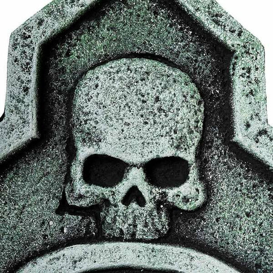 En närbild på den övre delen av gravstenen, som fokuserar på den stora, detaljerade dödskallen.