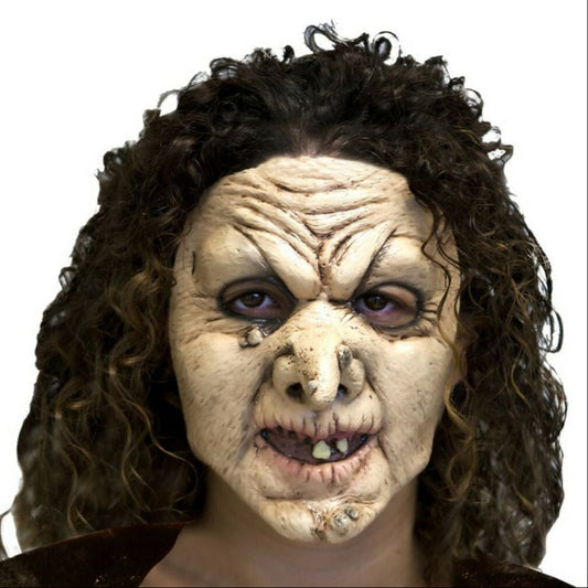 En närbild av en kvinna med mörkt, lockigt hår som bär en grotesk häxmask med en krokig näsa och en ondskefull blick.