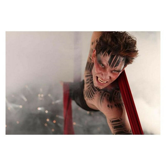 En man med intensiv blick och avancerad kroppsmålning visar upp sina realistiska Scarecrow-huggtänder medan han hänger i röda tyger.