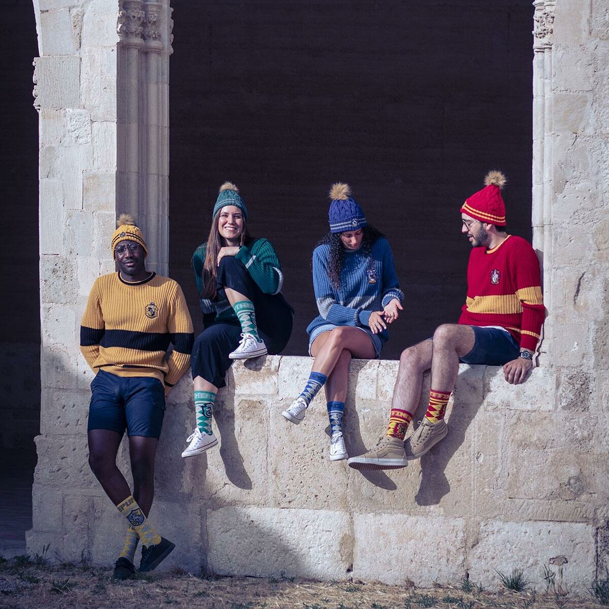 Fyra personer som representerar de olika Hogwarts-elevhemmen sitter tillsammans och bär sina respektive stickade mössor och tröjor.