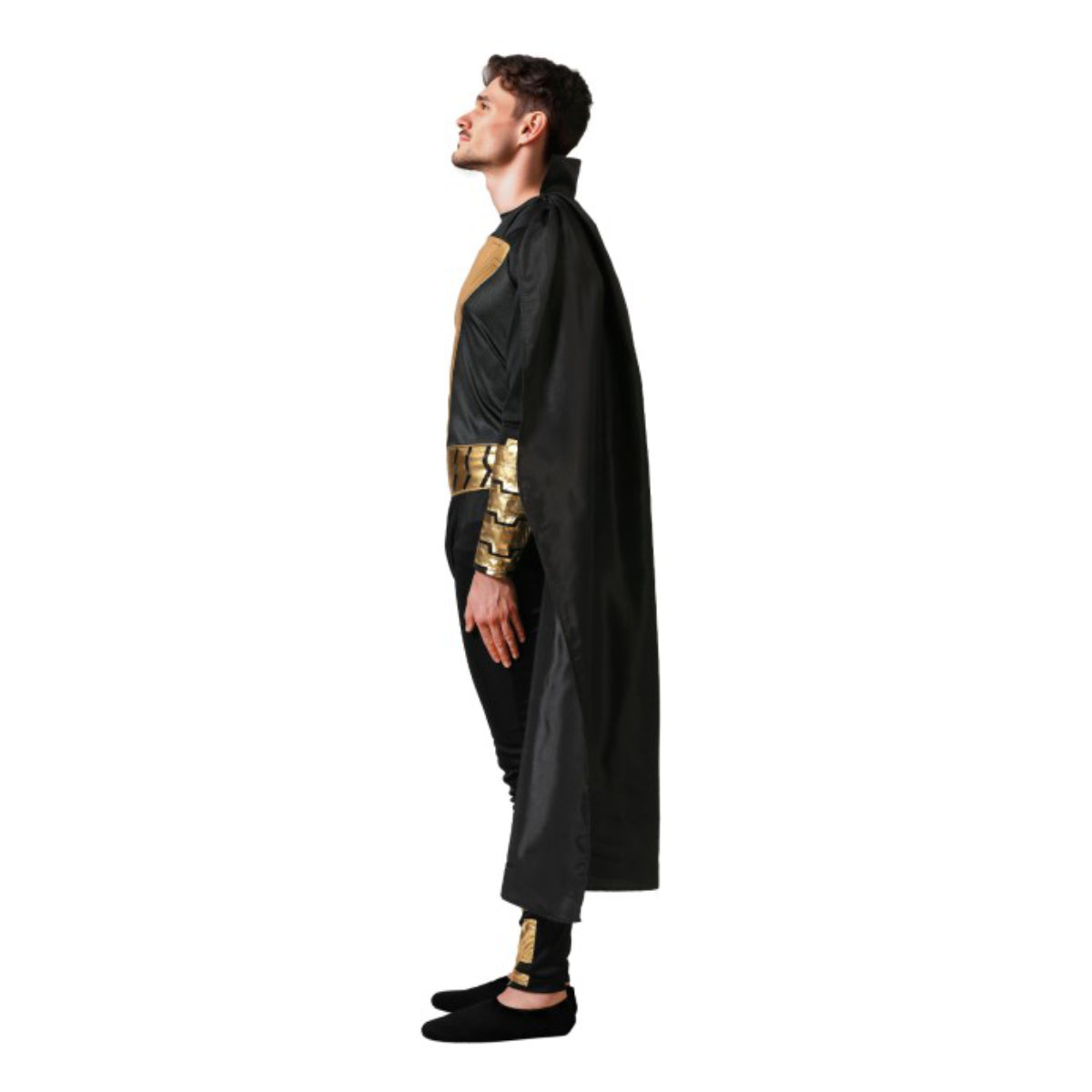 En man ses i profil, iklädd en svart och guldfärgad anti-hero-dräkt med en lång svart cape, och blickar stolt uppåt i en studio.