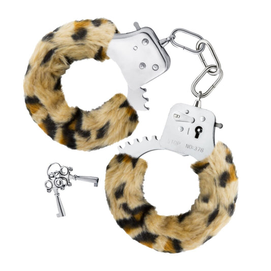 Två silverfärgade handfängsel fodrade med mjuk, brun och svart leopardmönstrad fuskpäls, med en kort kedja som länkar dem, samt ett set med två små nycklar ligger bredvid.