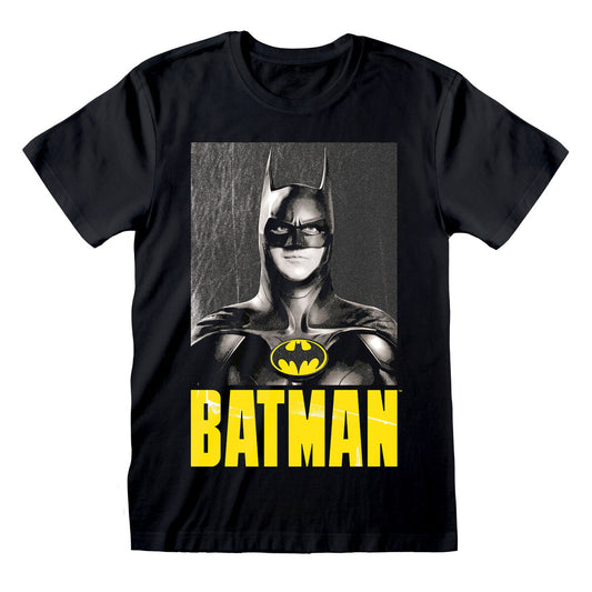 Närbild på en svart kortärmad unisex t-shirt med ett tryck av Michael Keaton som Batman i gråskala, med den gula Batman-logotypen och namnet "BATMAN" tryckt under i stora gula bokstäver.