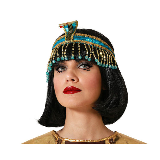En kvinna med svart page-peruk bär en egyptisk huvudbonad i turkost och guld med dinglande pärlor och en kobra i pannan.
