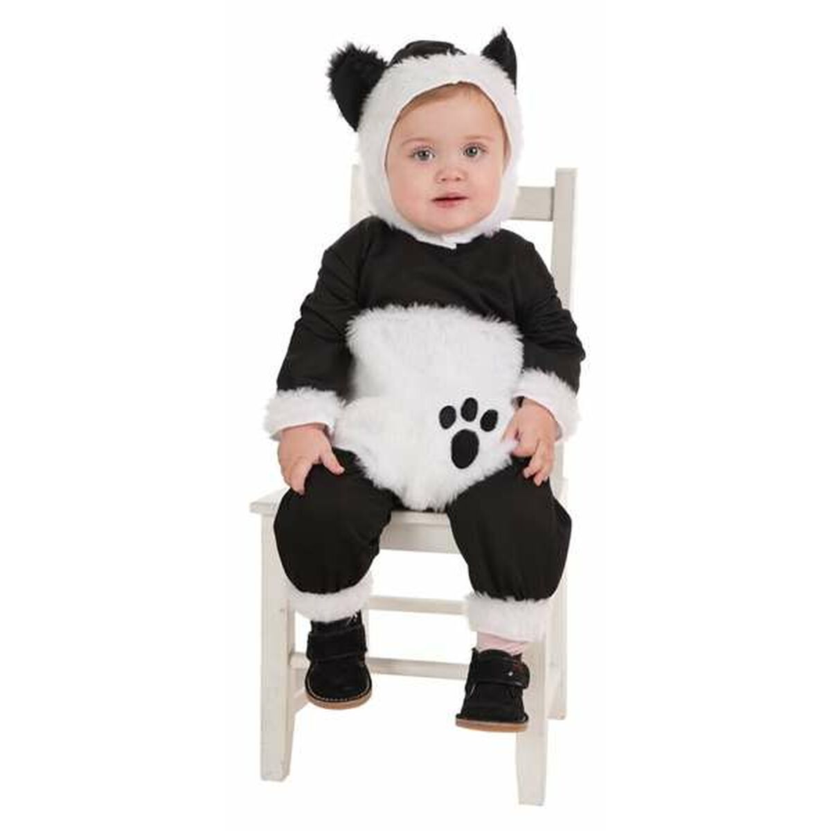 En baby sitter på en liten vit stol klädd i en svart och vit Gosepanda maskeraddräkt med en huva med öron och en vit mage med ett svart tassavtryck.