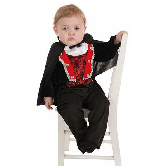 En baby sitter på en vit stol klädd i en svart och röd vampyrdräkt med en liten svart cape.