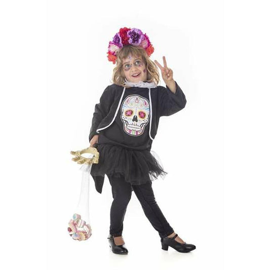 Ett barn poserar glatt i en svart Catrina-maskeraddräkt med en stor färgglad dödskalle på tröjan och en blomsterkrans på huvudet.