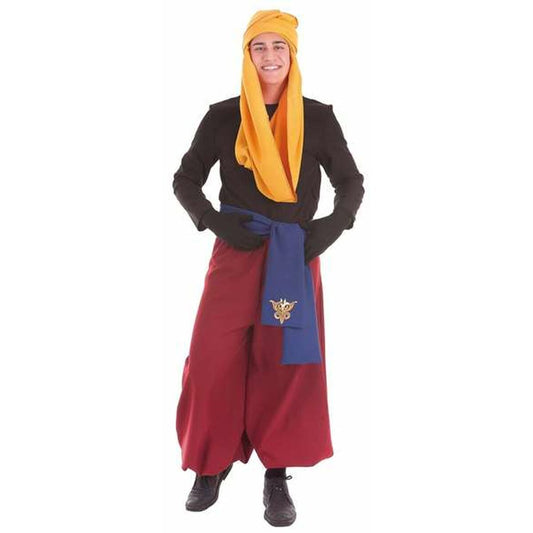 En man ler iklädd en maskeradkostym föreställande en arabisk prins eller pappersarbetare, med röda vida byxor, svart tröja, ett blått bälte med gulddetalj, svarta handskar och en stor gul turban.