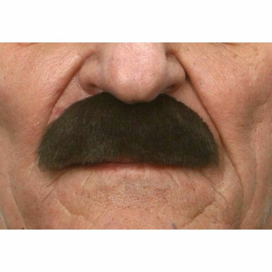Närbild på en mustasch i mörkt brunt/svart hår som är fastsatt ovanför överläppen på en äldre mans ansikte.