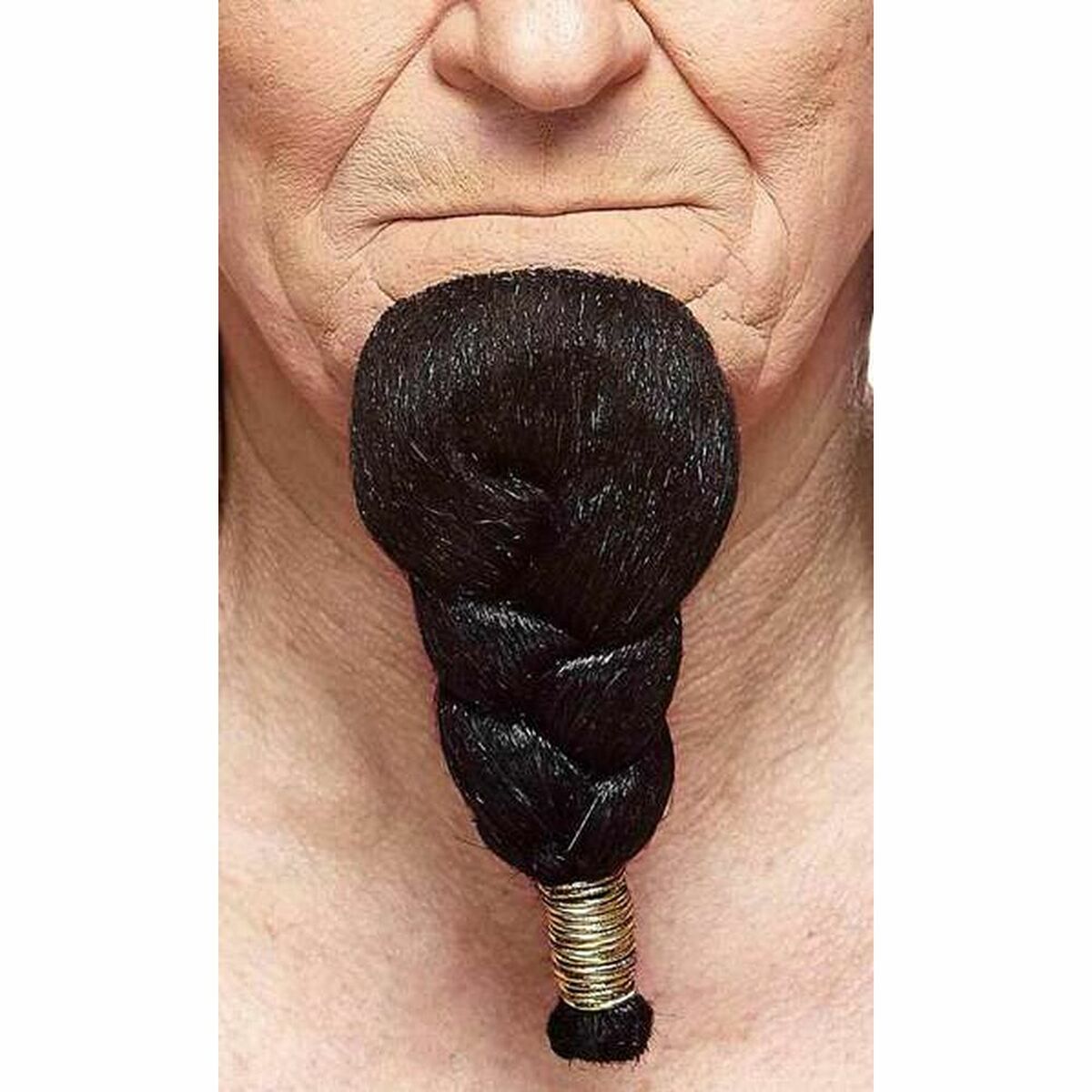 Närbild på en vuxen persons haka där en tjock, svart, flätad hakskäggsaccessoar sitter fast, avslutad med flera tunna guldiga ringar.