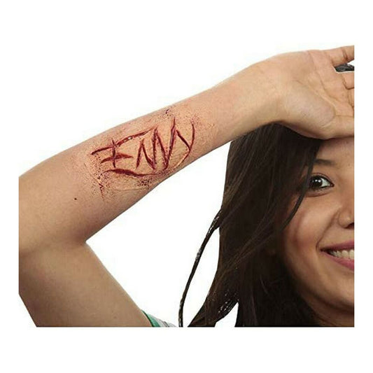En person visar upp en realistisk latex-tatuering på underarmen där ordet 'ENVY' är inristat med blodröd färg.