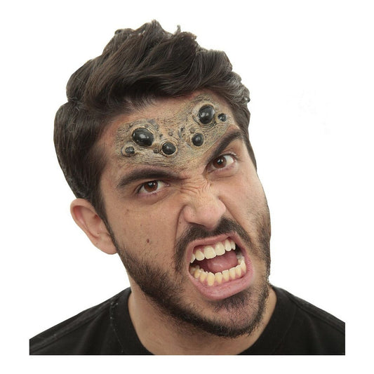 Närbild på en man med intensivt ansiktsuttryck som har på sig en latexmaskeradaccessoar föreställande en samling svarta spindelögon ovanför ögonbrynen.