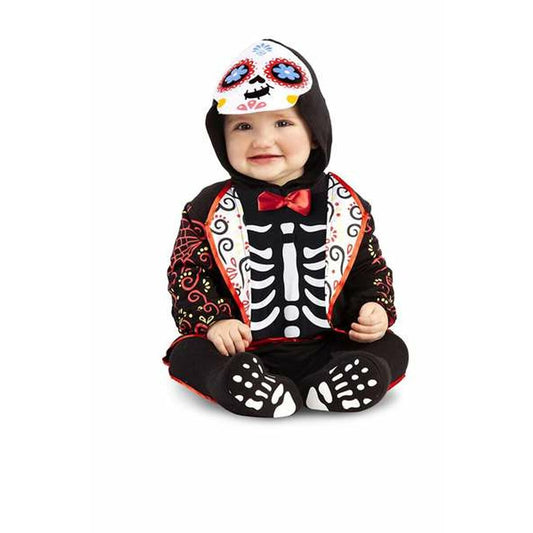 En glad bebis sitter ner i en svart maskeraddräkt som föreställer ett skelett i Día de Muertos-stil, med en huva som har ett färgglatt sockerhuvudsmotiv.