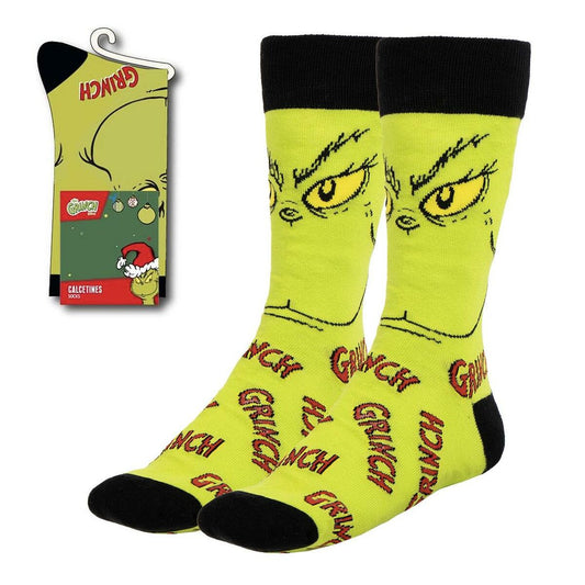 Ett par limegröna unisex-strumpor med tryck av Grinchs ansikte och ordet GRINCH på foten, förpackade med en etikett som visar Grinch.