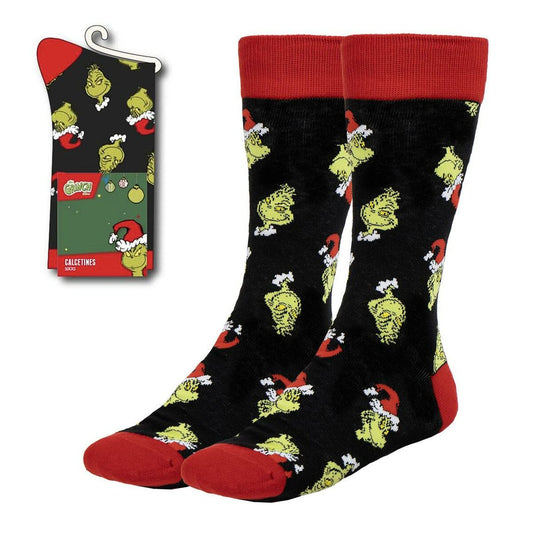 Ett par svarta strumpor med ett mönster av den gröna karaktären Grinch i tomteluva, med röda tår och muddar, visas bredvid sin förpackning.