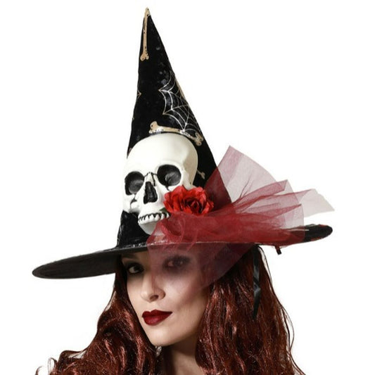 En kvinna bär en svart, spetsig häxhatt dekorerad med en vit dödskalle, ett rött tygros och röda tyll-detaljer, perfekt för Halloween.
