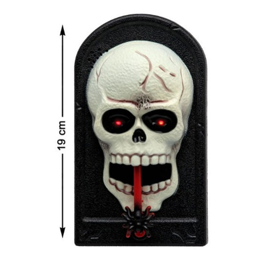 En närbild på en svart, rektangulär halloweendekoration som föreställer ett vitt skallehuvud med glödande röda ögon, en röd tunga hängandes ut ur munnen och en liten svart spindel längst ner.