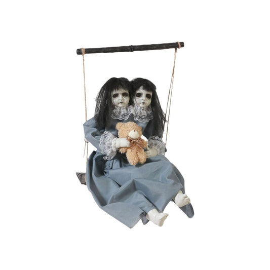 En skrämmande Halloween-dekoration som visar en docka med dubbla huvuden sittandes på en gunga och håller i en brun nallebjörn.
