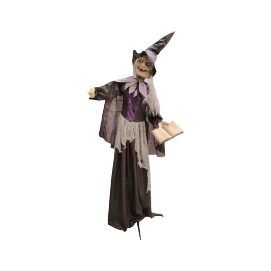 En stor, animerad halloweendekoration föreställande en skrämmande häxa i svart och lila dräkt som håller i en öppen bok.