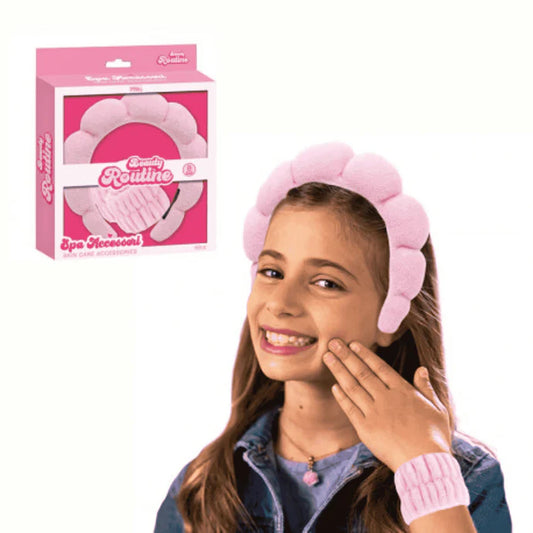 En glad tjej bär ett tjockt, mjukt rosa diadem med fluffiga kuddar och ett matchande handledsband medan hon rör vid sitt kind.