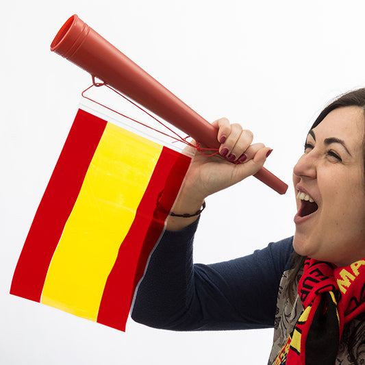 En kvinna blåser högt i en röd plasttrumpet som har en spansk flagga fäst vid sig.