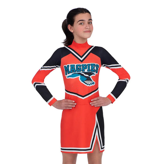 En närbild på en självsäker flicka poserar med händerna på höfterna, iklädd en orange och svart långärmad cheerleaderdräkt för barn.