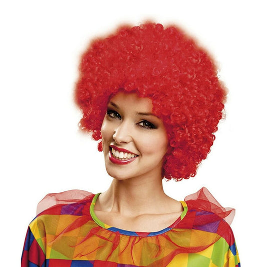 En leende kvinna i en färgglad clowndräkt bär en stor, yvig och superkrullig peruk i en intensiv, eldröd färg.