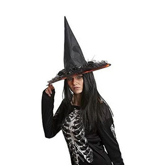 En kvinna med långt, mörkt hår och en skelettröja bär en spetsig, svart häxhatt som är elegant dekorerad med svarta rosor och tyll runt brättet.