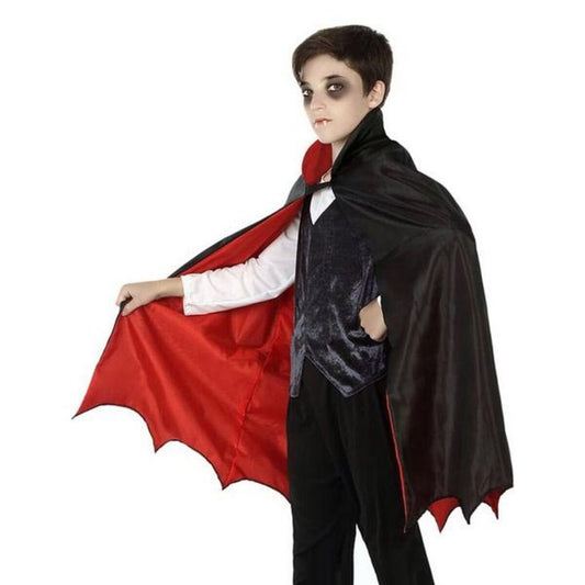 En pojke med mörkt smink runt ögonen poserar i en elegant, svart vampyrmantel för barn, och visar upp det röda fodret och den höga kragen.