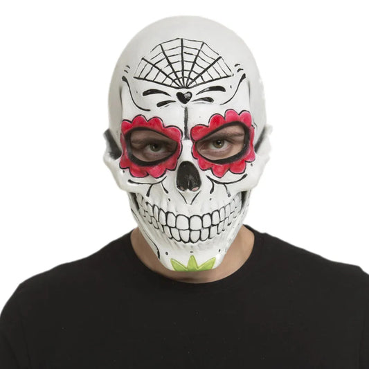 En man med intensiva ögon bär en vit Day of the Dead-mask, dekorerad med röda blommor runt ögonen och ett svart spindelnät målat i pannan.