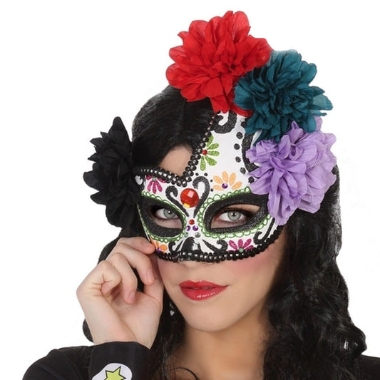 En kvinna med en intensiv blick bär en vacker, vit Day of the Dead-ögonmask dekorerad med svarta mönster, glitter och en stor krans av färgglada tygblommor.