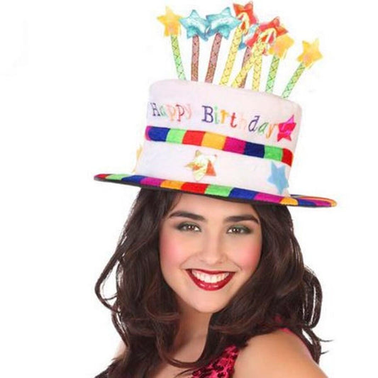 En leende kvinna bär en hög, vit Festlig Födelsedagstårta Hatt med texten "Happy Birthday" och färgglada ljus på toppen.