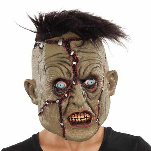 En person bär en heltäckande latexmask som föreställer Frankies monster, med grönaktig hud, tydliga ärr med stygn över hela ansiktet, stirrande blå ögon och en spretig svart kalufs.