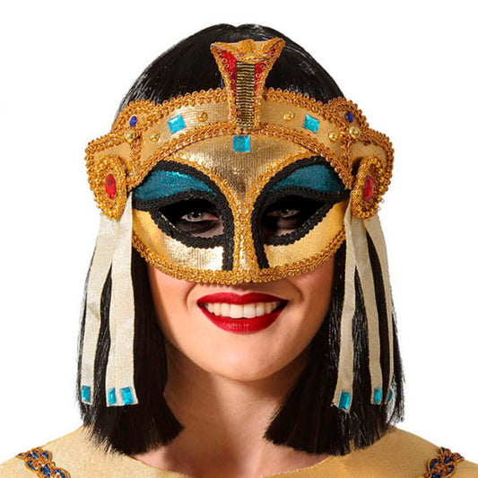 En leende kvinna med kort, svart hår bär en storslagen och detaljerad egyptisk farao-ögonmask i guld, dekorerad med juveler och en kobra.