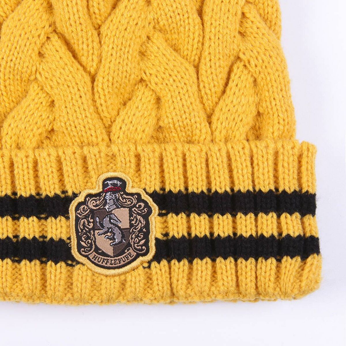 Framsidan av den stickade Hufflepuff-mössan som visar det broderade grävling-emblemet på den randiga kanten.