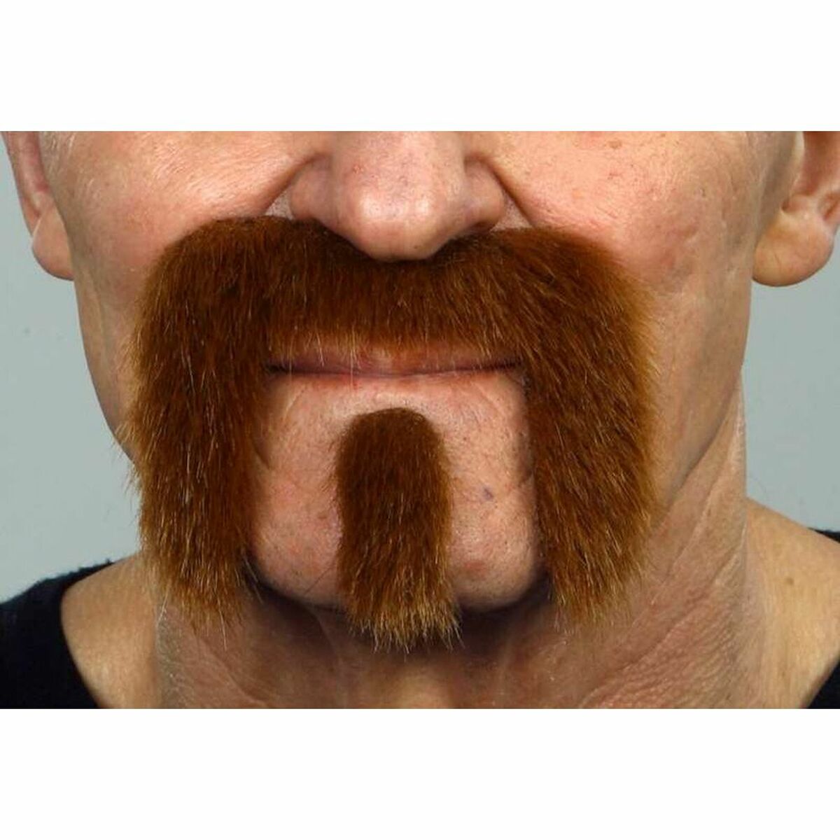 Närbild på en mans ansikte där en kastanjebrun, tjock mustasch och hakskägg i biker/skurk-stil är fastklistrad på huden.