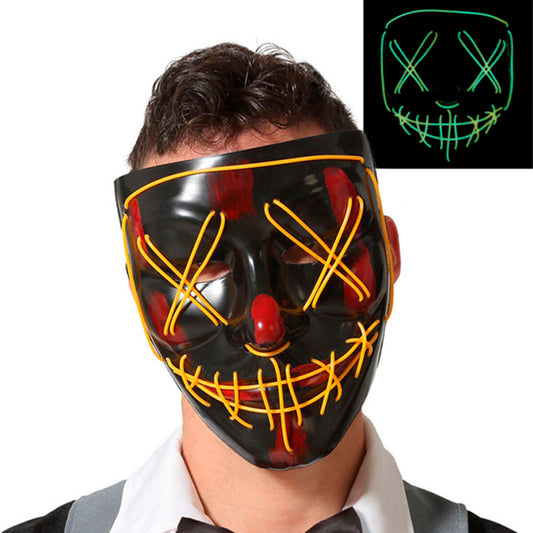 Man med svart LED-mask med korsade gula lysande trådar över ögonen och munnen, visar även masken i mörker med starkt grönt sken.
