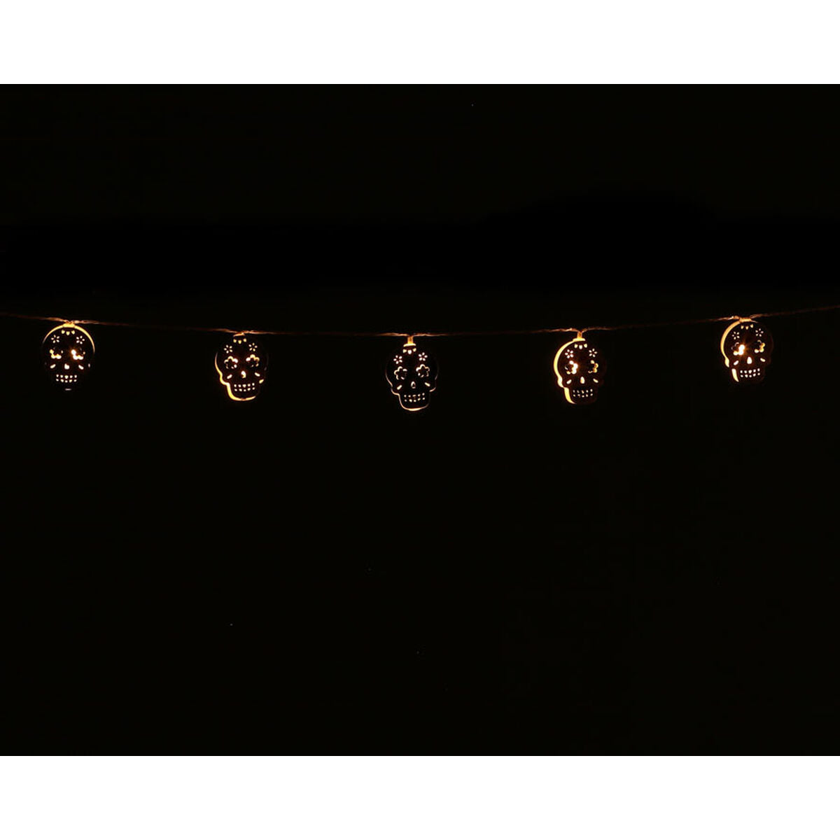 En ljusslinga med utskurna dödskallar som lyser med ett varmt, gult sken i mörkret, perfekt som halloweendekoration.