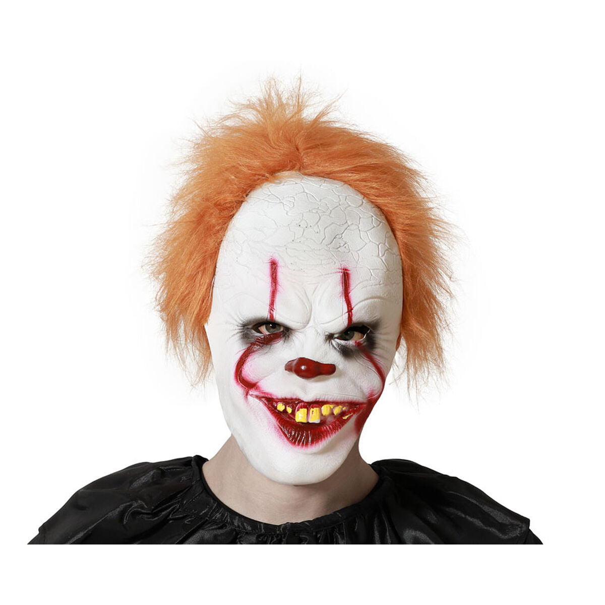 En person bär en skräckinjagande, heltäckande clownmask med ett vitt, sprucket ansikte, spretigt orange hår, ett ondskefullt leende med gula tänder och röda streck över ögonen.