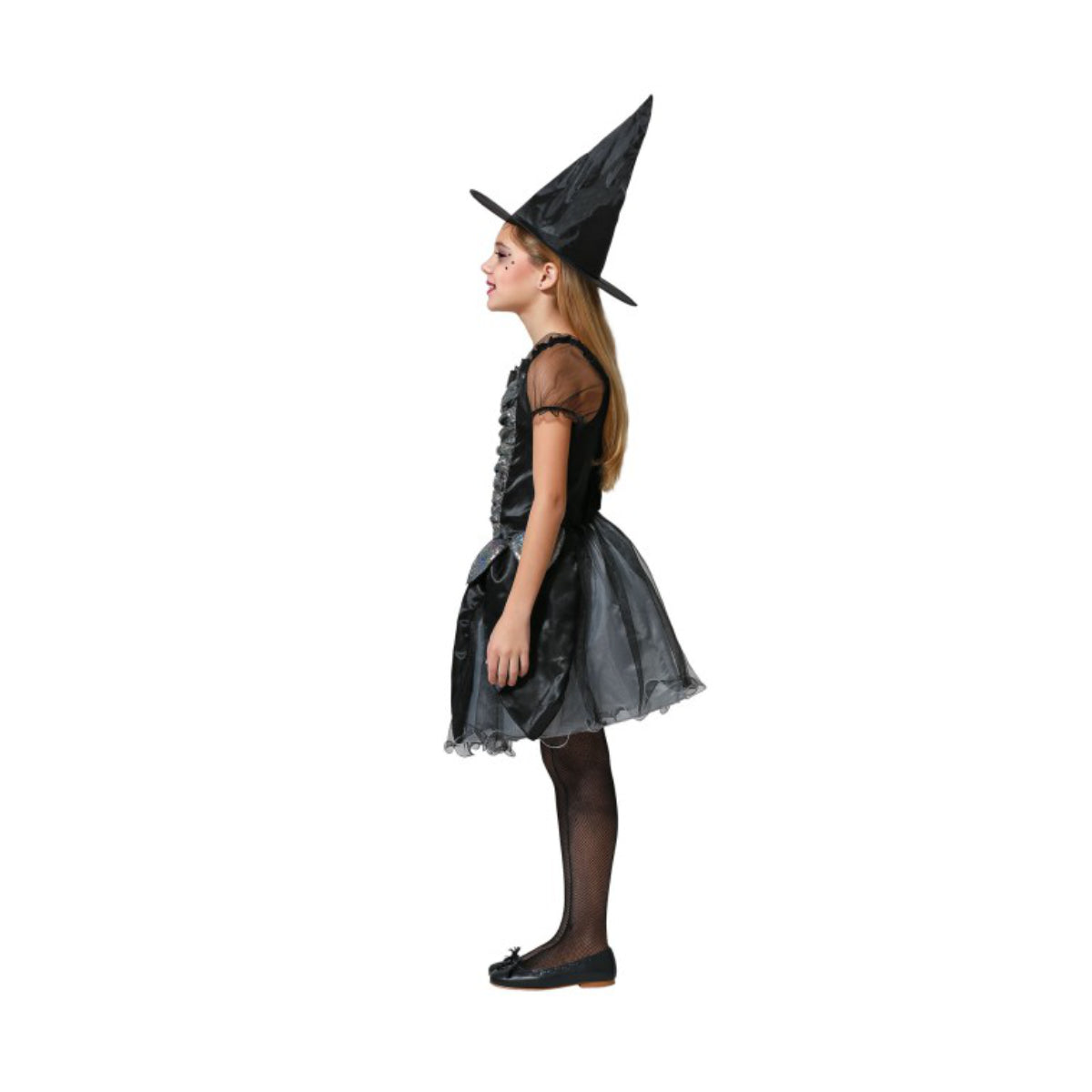 En flicka ses i profil, iklädd en svart och silverskimrande häxdräkt för barn med en spetsig häxhatt och nätstrumpbyxor, fotograferad mot en vit bakgrund.